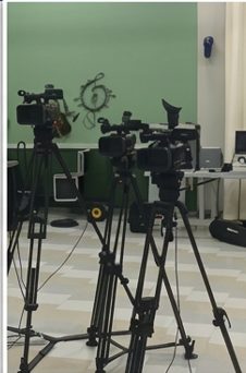 Three studio cameras on tripods in front of a green wall